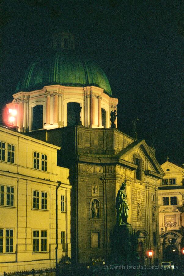 Night view of a historic church and surrounding buildings in Prague, illuminated against the dark sky