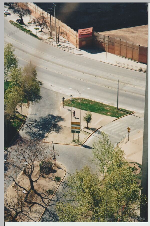 High-angle view of a wide avenue in Ñuñoa with sidewalks, green areas, a bus stop sign, traffic barriers, and a fenced deep-excavation site
