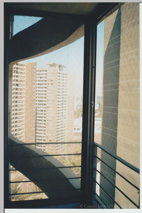 View from a high-rise apartment balcony in Ñuñoa toward neighboring residential towers, framed by railings, safety netting, and the building’s concrete structure