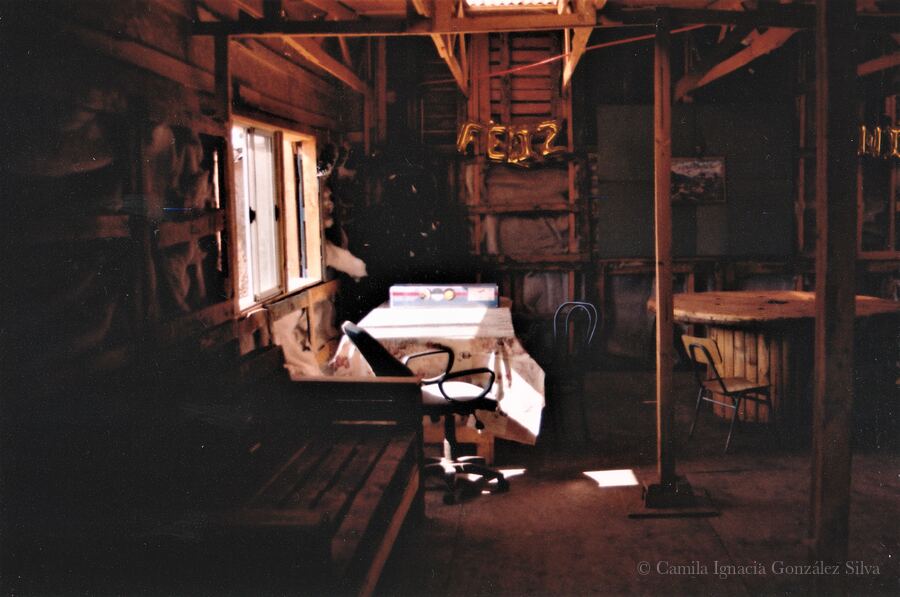 Interior of Cootramap’s 2022 self-built headquarters in La Pintana, with wooden walls, exposed beams, tables, chairs, and daylight entering through a side window