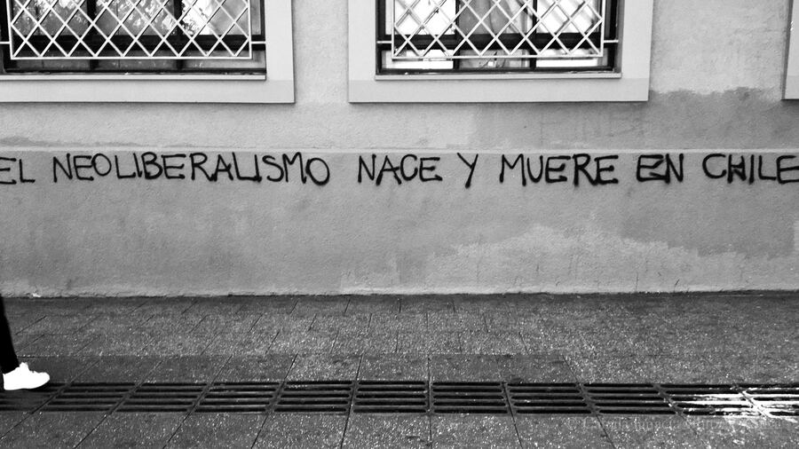 Wall in Santiago de Chile with barred windows and a protest graffiti reading 'El neoliberalismo nace y muere en Chile'