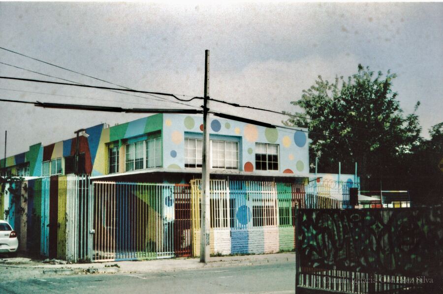 Analogue photograph of a kindergarten in Puente Alto with colorful geometric façades, polka-dot walls, perimeter fencing, and overhead wiring