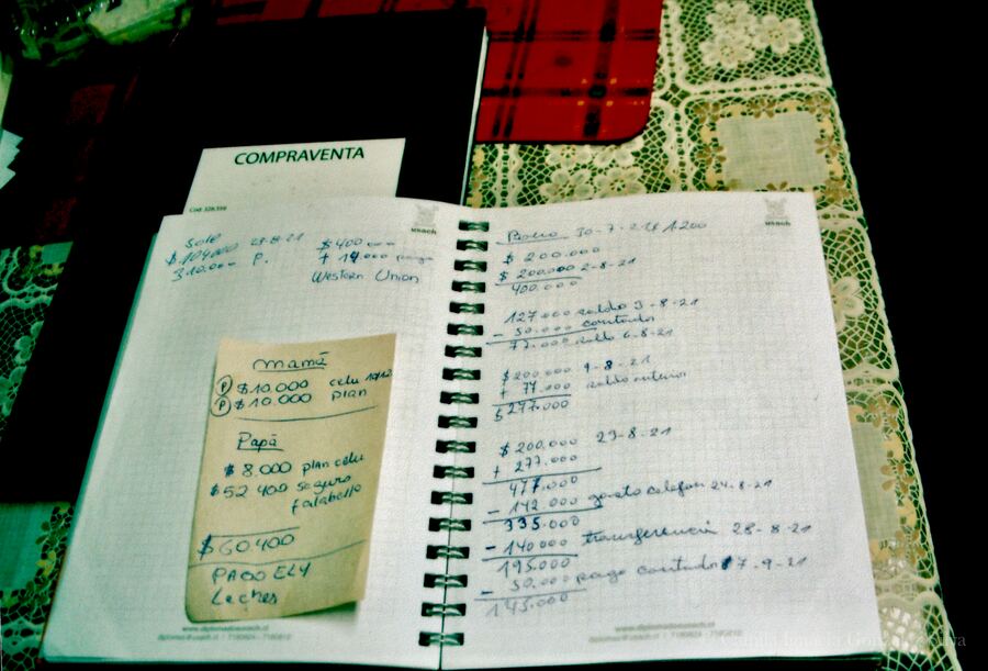 Analogue photograph of an open notebook with handwritten household accounts, debts, and payment notes on a table in Santiago, Chile