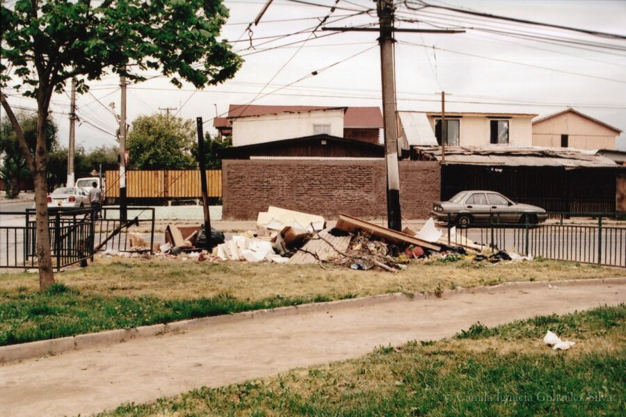 Neighborhood green space in Puente Alto with dumped debris, surrounding housing, and dense overhead wiring